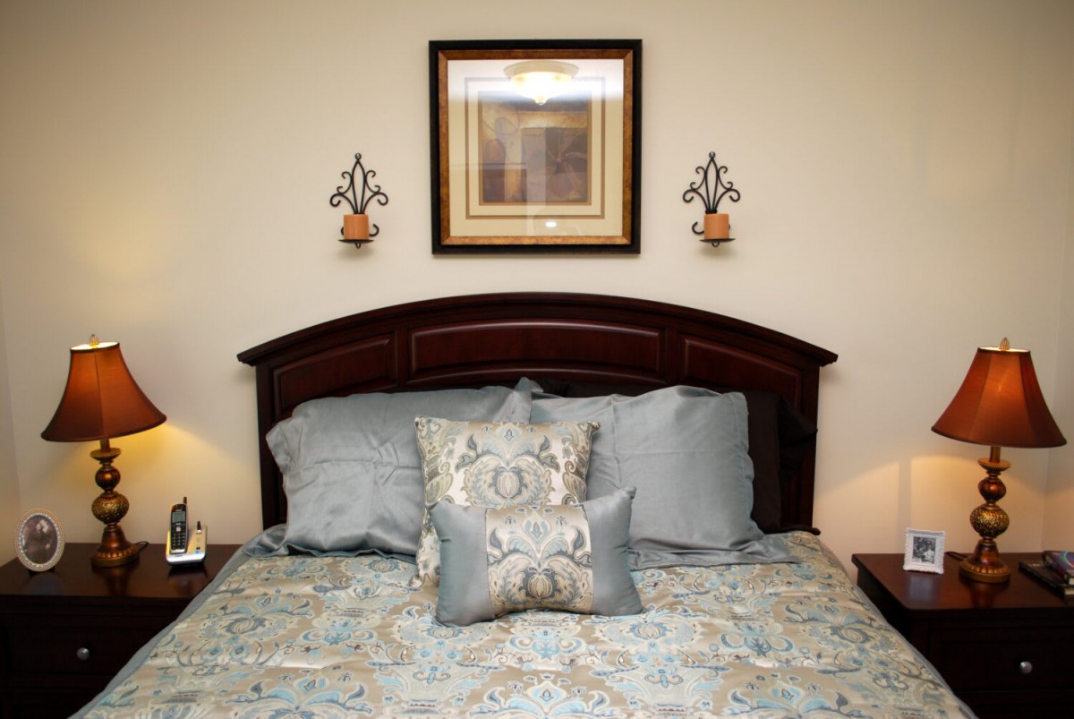 A well-decorated bedroom with a neatly made bed, featuring multiple pillows and a framed artwork above the headboard.