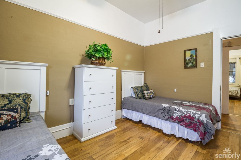 A cozy bedroom with two twin beds, a white dresser, and wooden flooring. A plant sits atop the dresser, adding a touch of greenery to the room.