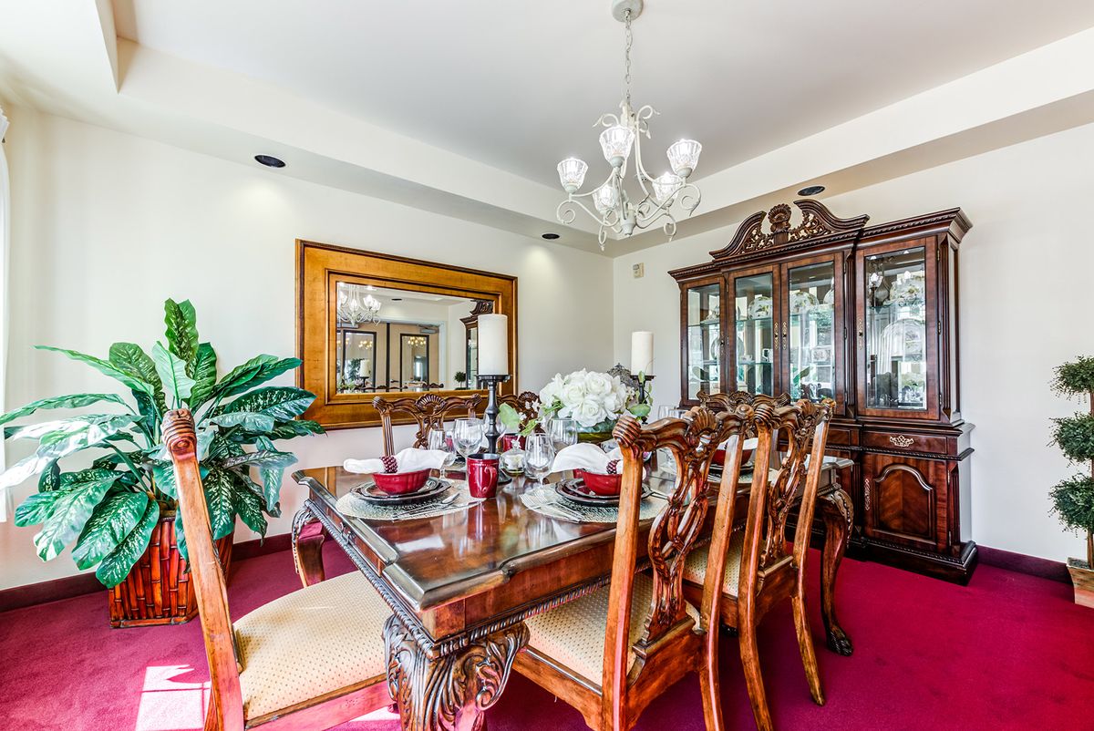 An elegant dining room with a polished wooden table, ornate chairs, and a chandelier.