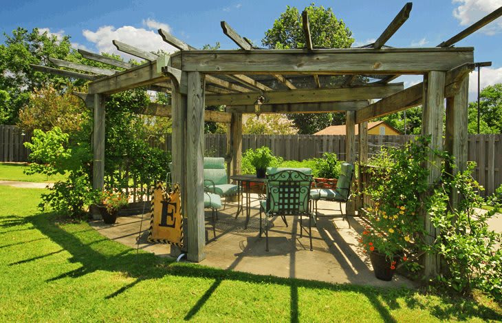A sunny garden with a pergola and comfortable outdoor seating surrounded by lush greenery.