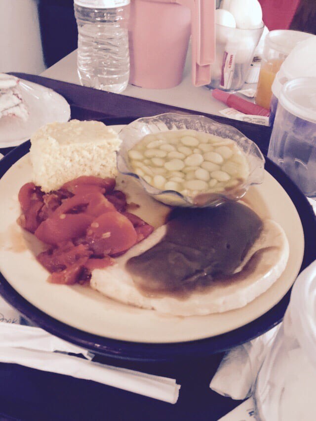 A plate of food featuring sliced tomatoes, a serving of mashed potatoes, a bowl of green peas, and gravy-covered meat.