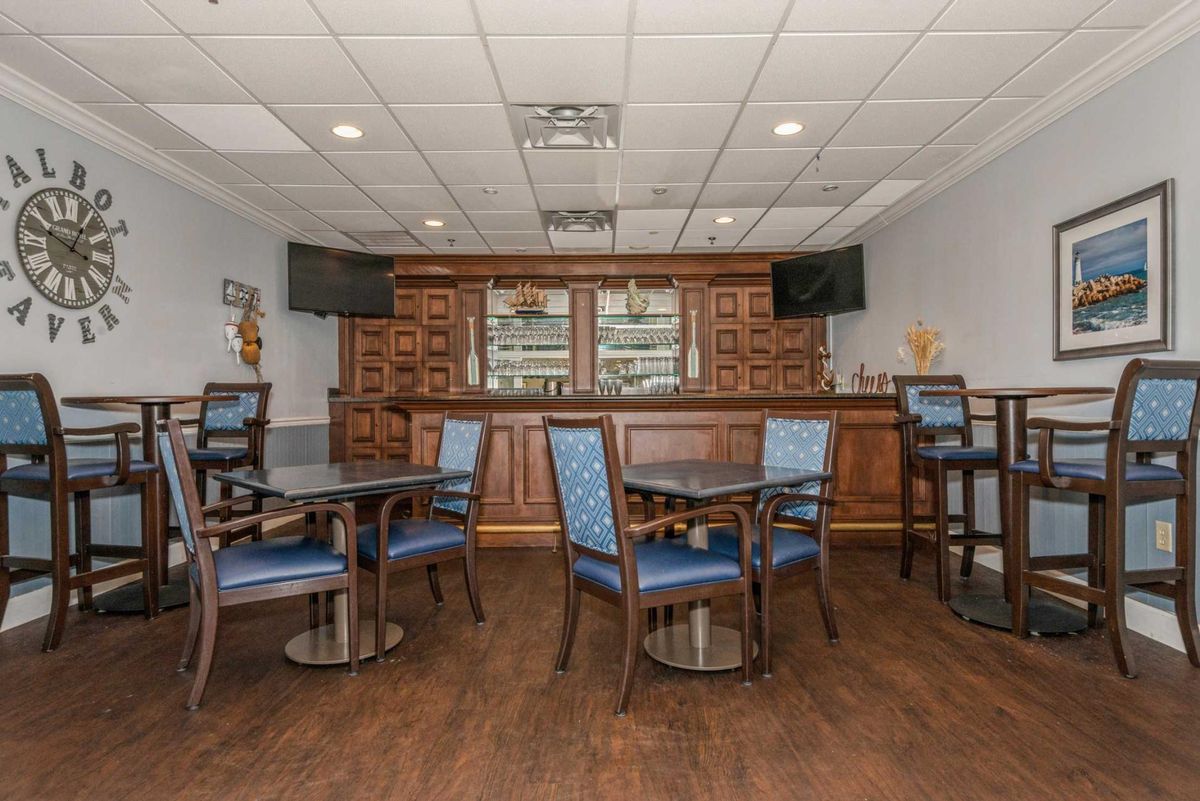 A cozy bar area featuring wooden tables and chairs, with televisions mounted on the walls.