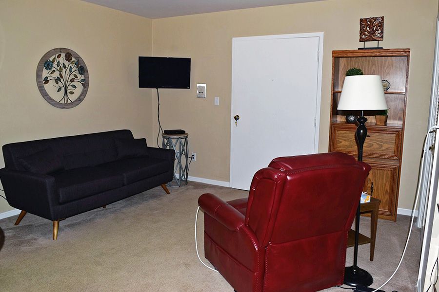 A cozy living room featuring a black sofa, red armchair, wall-mounted television, and a clock.