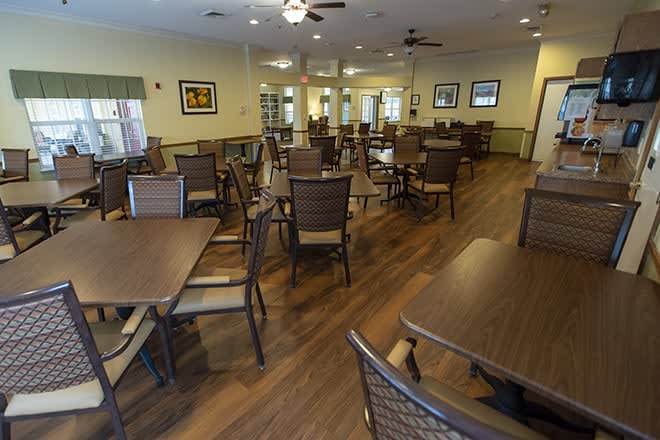 A spacious dining area with neatly arranged tables and chairs on a wooden floor.