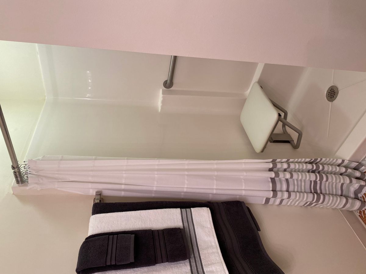 An accessible shower with a grab bar and folding chair, featuring neatly arranged towels.