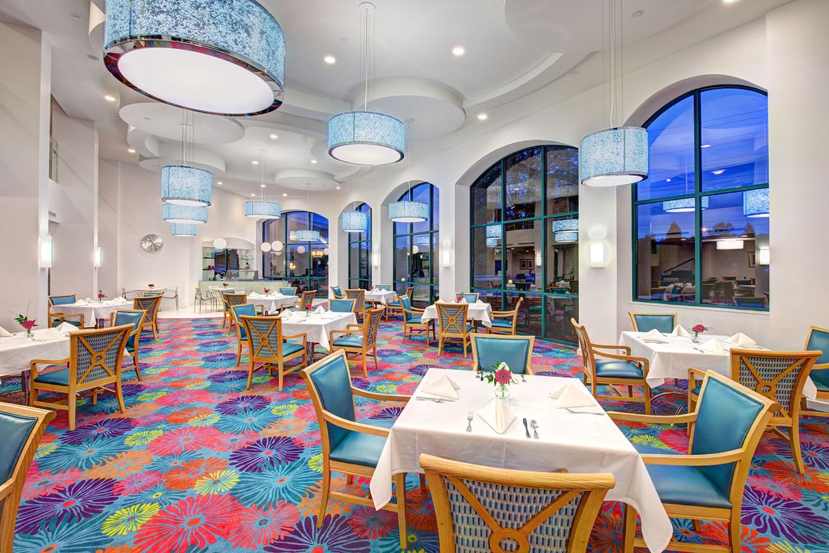 A vibrant restaurant interior with colorful carpet, modern furnishings, and large windows.