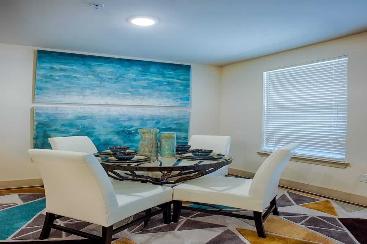 A modern dining room with a glass table, white chairs, and ocean-themed artwork on the wall.