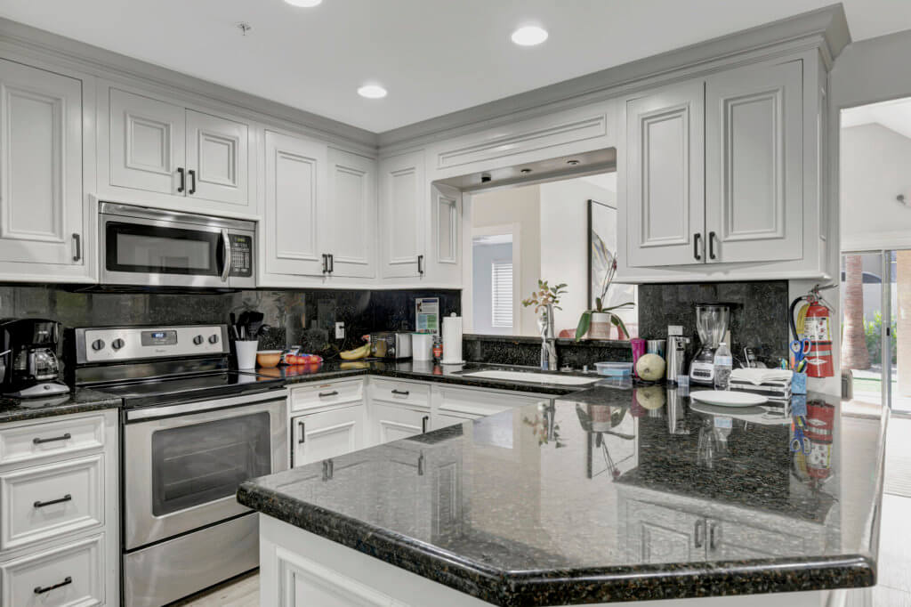 A modern kitchen with white cabinets and granite countertops, featuring stainless steel appliances.