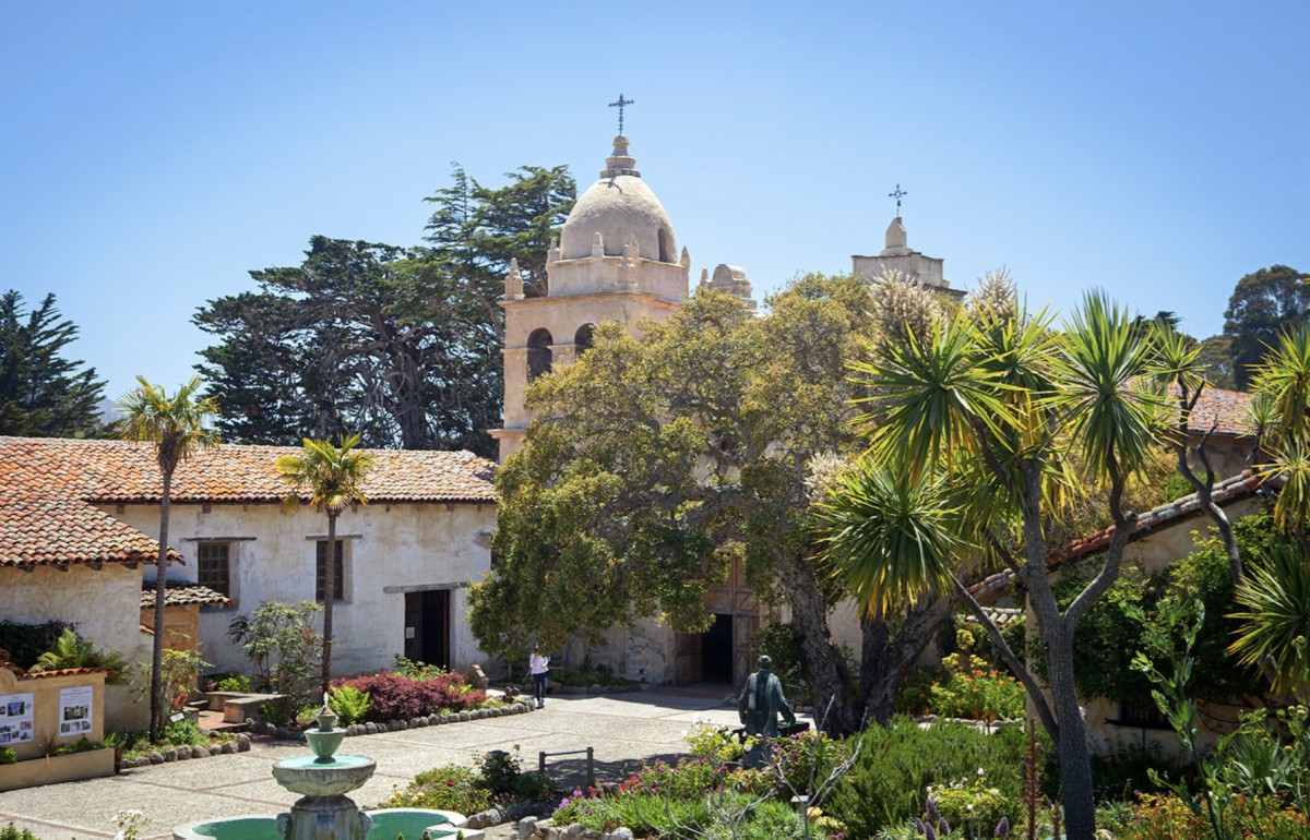 Historic mission church surrounded by trees and a fountain in California.