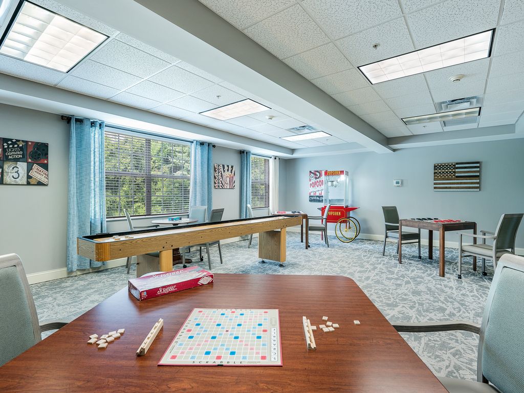 A bright and spacious game room featuring tables for board games and a shuffleboard setup.