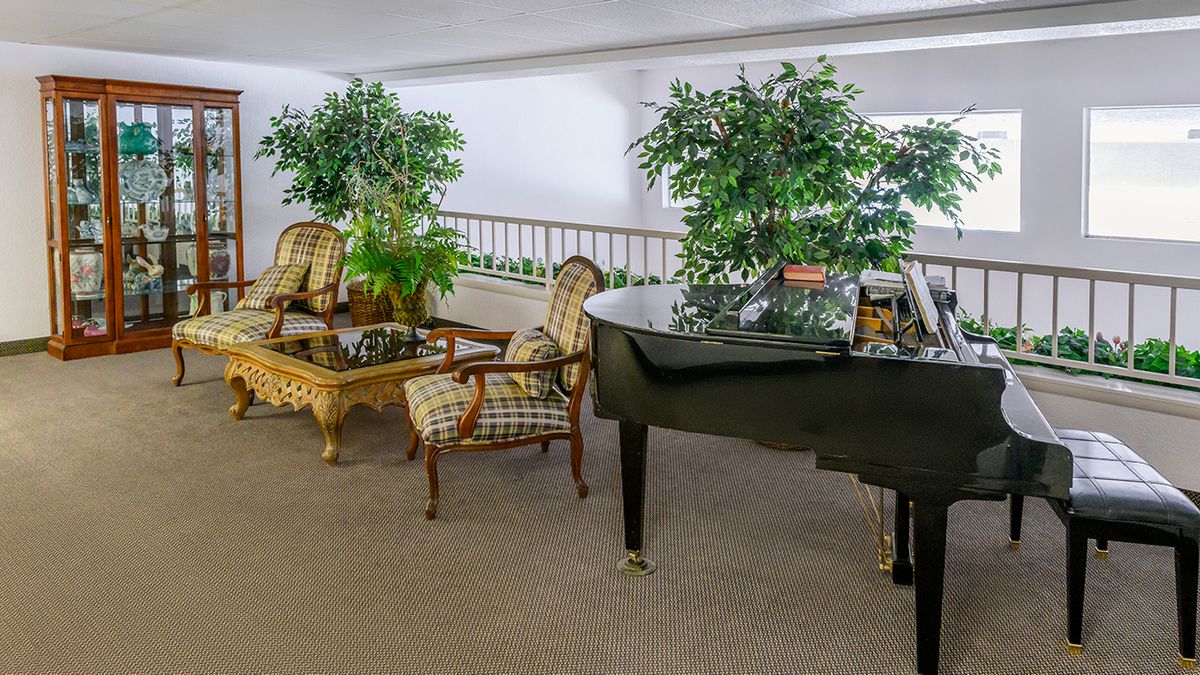 A cozy lounge area featuring a grand piano, surrounded by comfortable chairs and lush green plants.