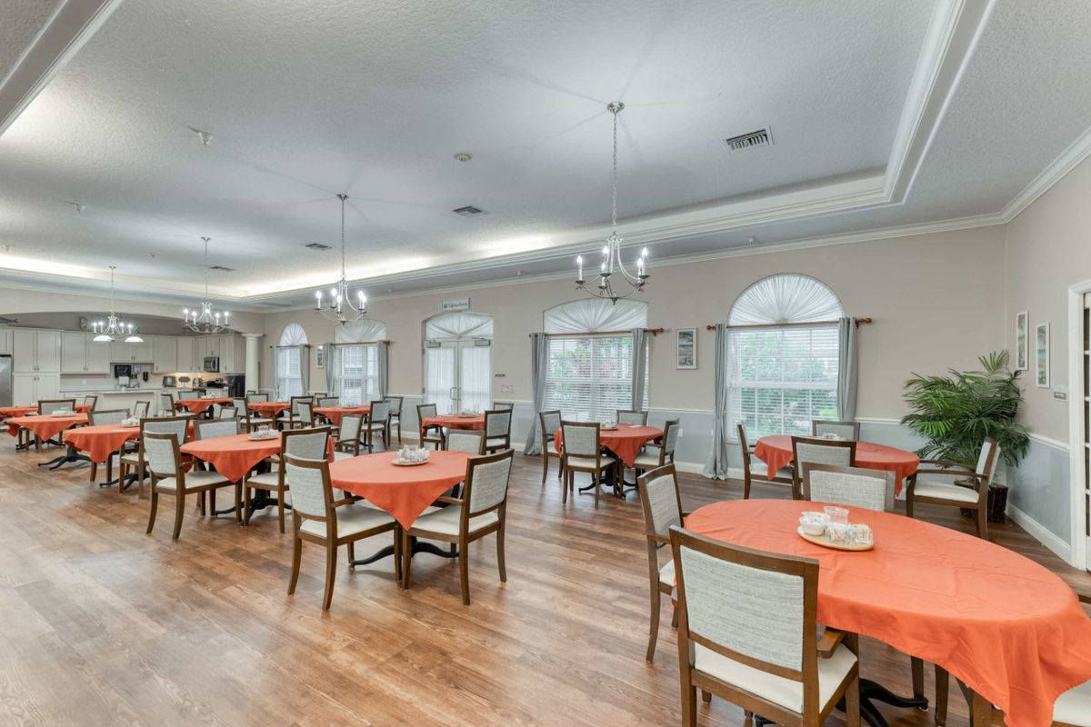 A spacious dining room with tables covered in orange tablecloths and elegant chandeliers.