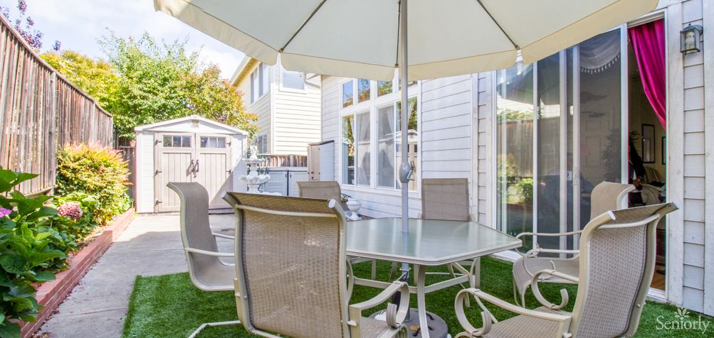 A cozy outdoor patio setup with a glass table and chairs under a large umbrella.