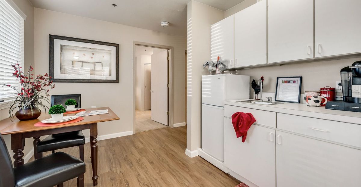 A compact kitchen with integrated laundry facilities, featuring white cabinets and wood flooring.