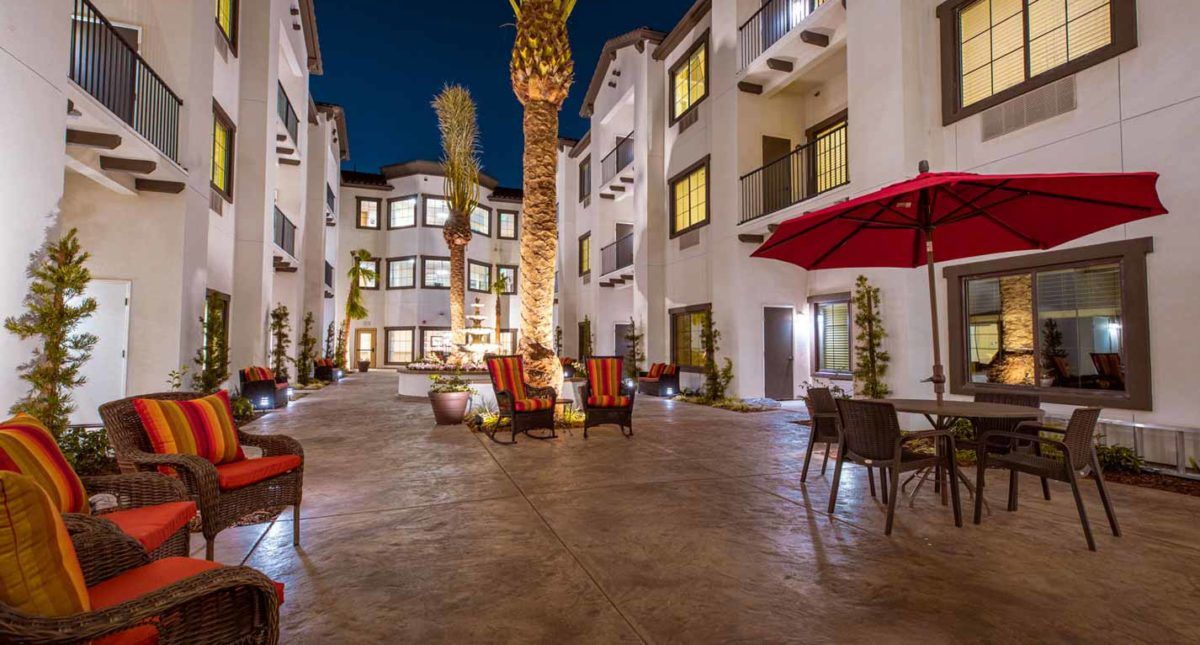 A well-lit courtyard in an apartment complex featuring palm trees and outdoor seating at night.