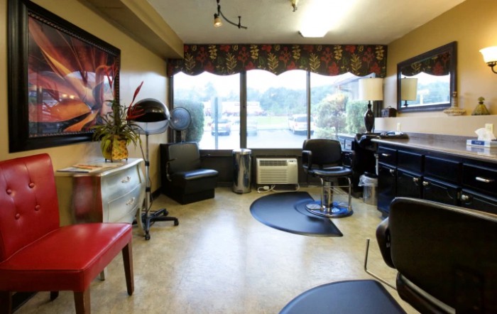 A cozy hair salon interior with chairs, a large window, and styling equipment.