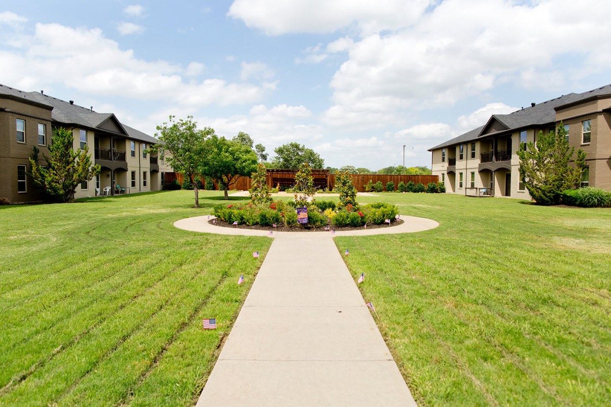 A serene garden with a central circular planter surrounded by grass and flanked by buildings on either side.