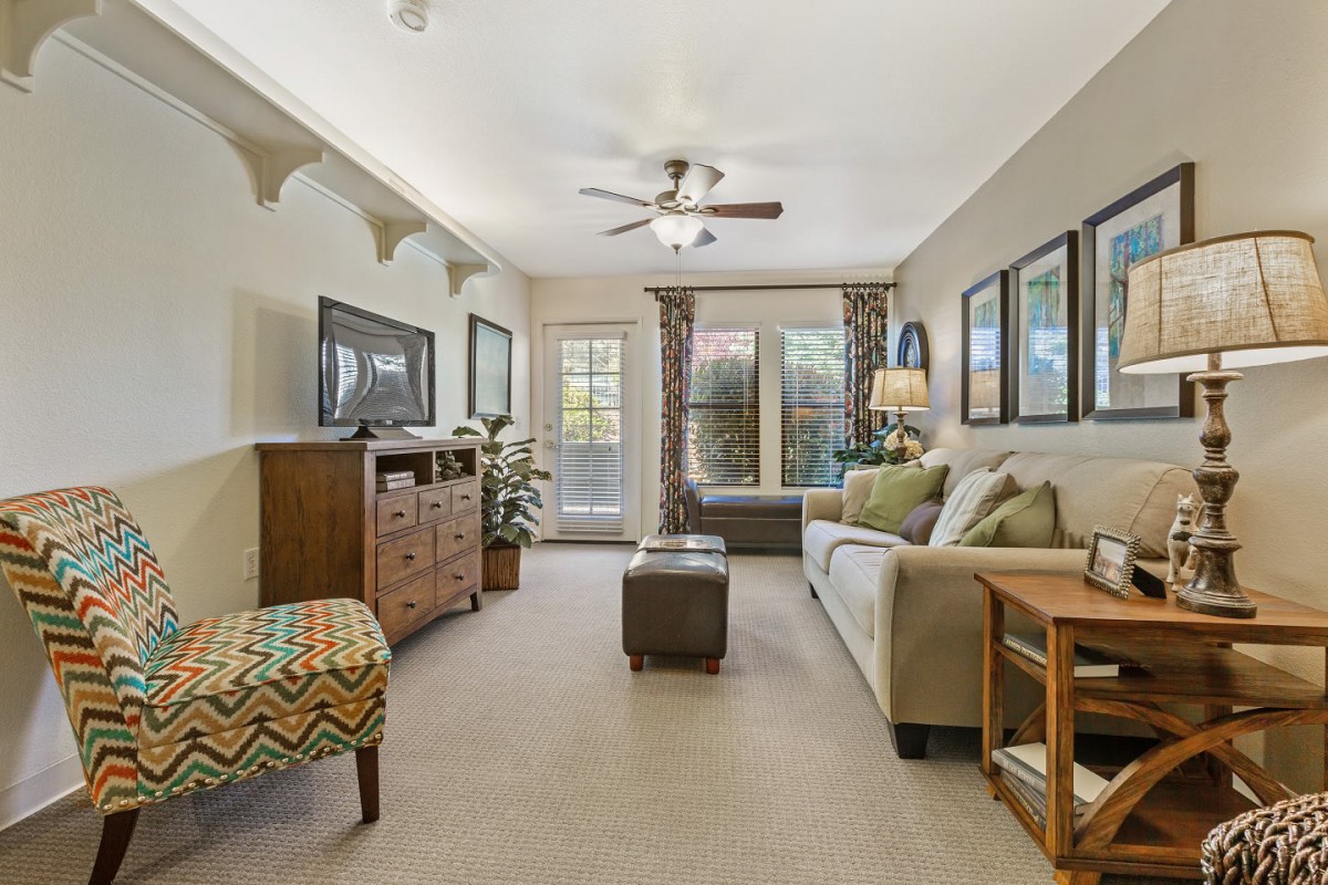 A cozy and thoughtfully decorated living room with a sofa, artwork on the walls, and a ceiling fan.