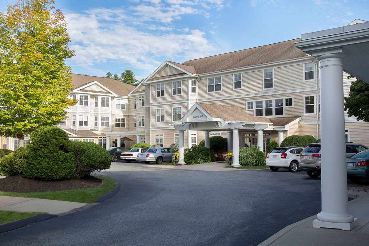 A residential building with a parking lot and driveway, surrounded by trees and under a partly cloudy sky.