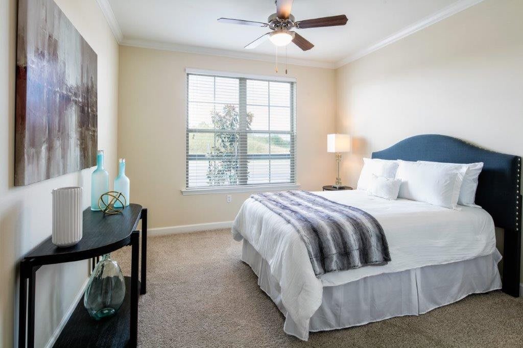 A neatly arranged bedroom with a large window, ceiling fan, and elegant decor.