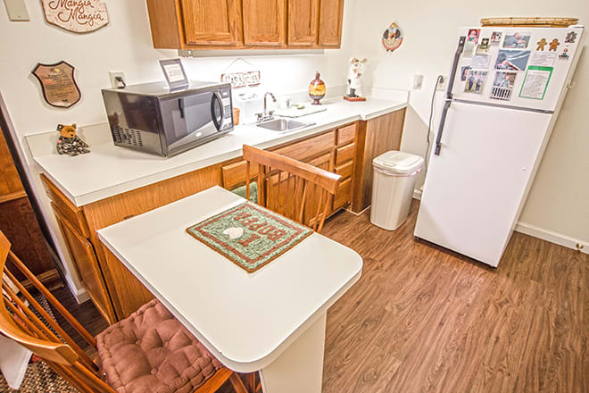 A small kitchen with wooden cabinets, a microwave, and a refrigerator, featuring a table and chairs.