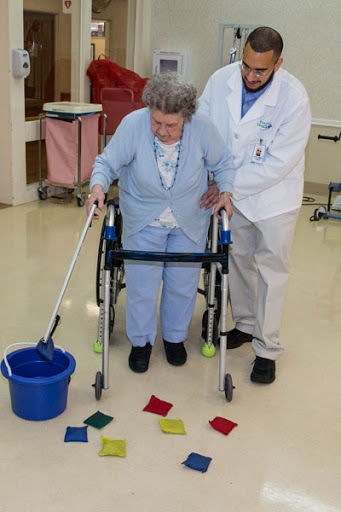 A healthcare professional assists an elderly patient in a rehabilitation activity using colorful tiles.