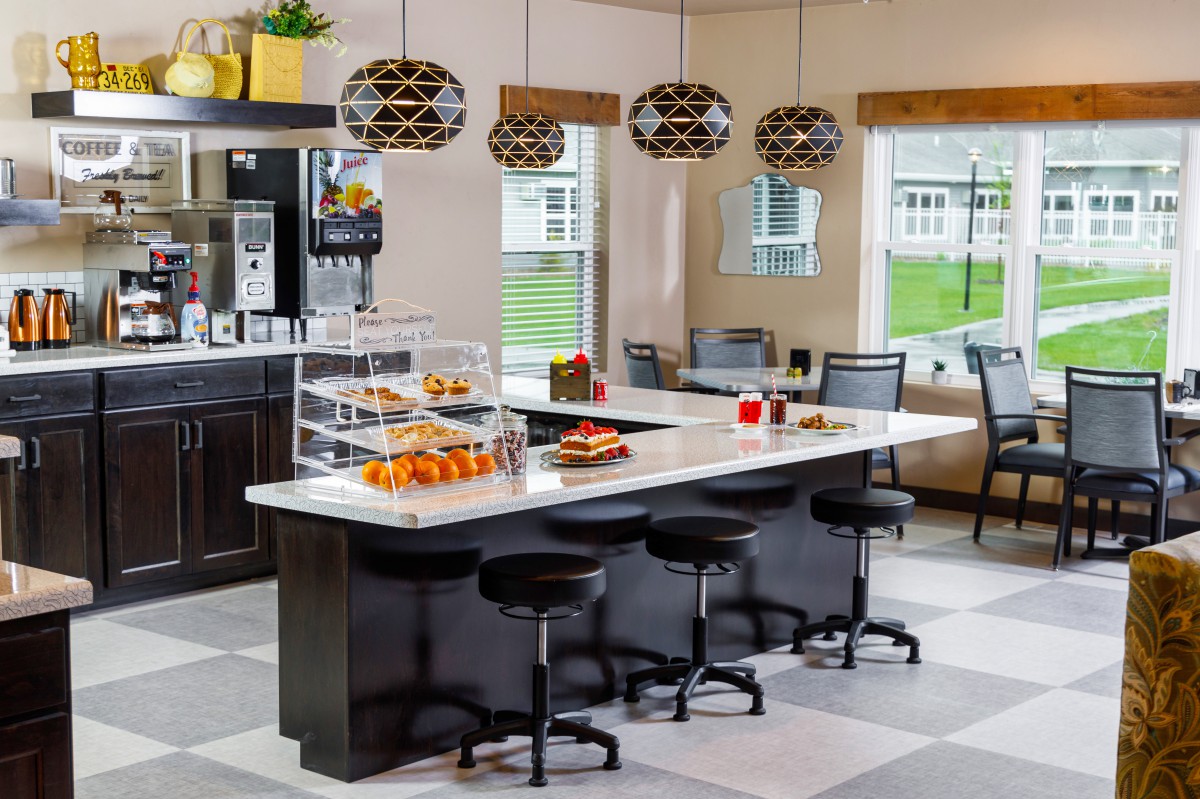 A modern kitchen with an island counter, stylish bar stools, and a display of pastries under geometric pendant lights.