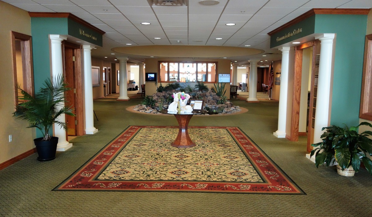 A spacious lobby with a decorative centerpiece on a round table, flanked by columns and featuring a green carpet.