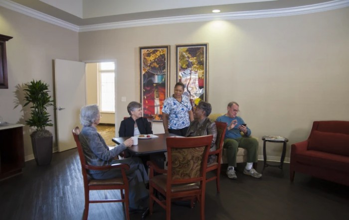 A group of people, including seniors and a staff member, are seated around a table in an indoor setting.