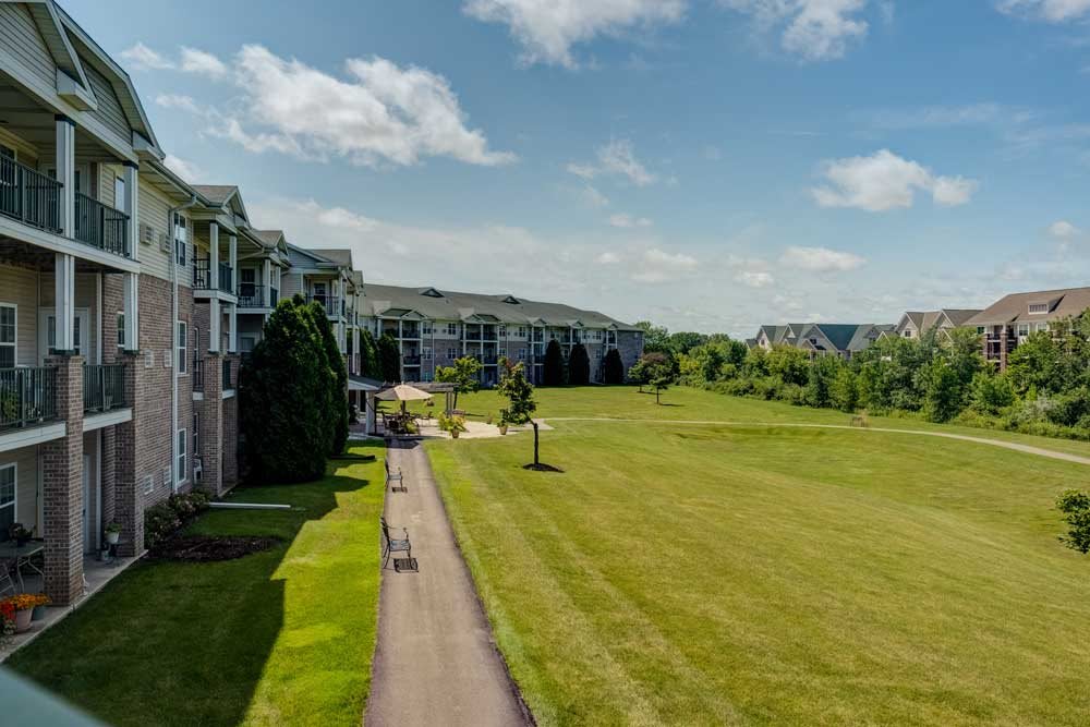 A scenic view of apartment buildings alongside a grassy open field with a pathway under a clear blue sky.