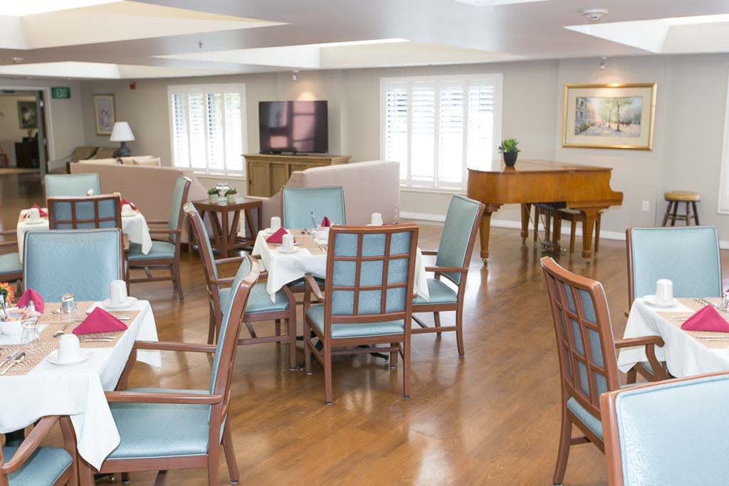 An empty dining room with neatly arranged tables and chairs, featuring a piano in the corner.
