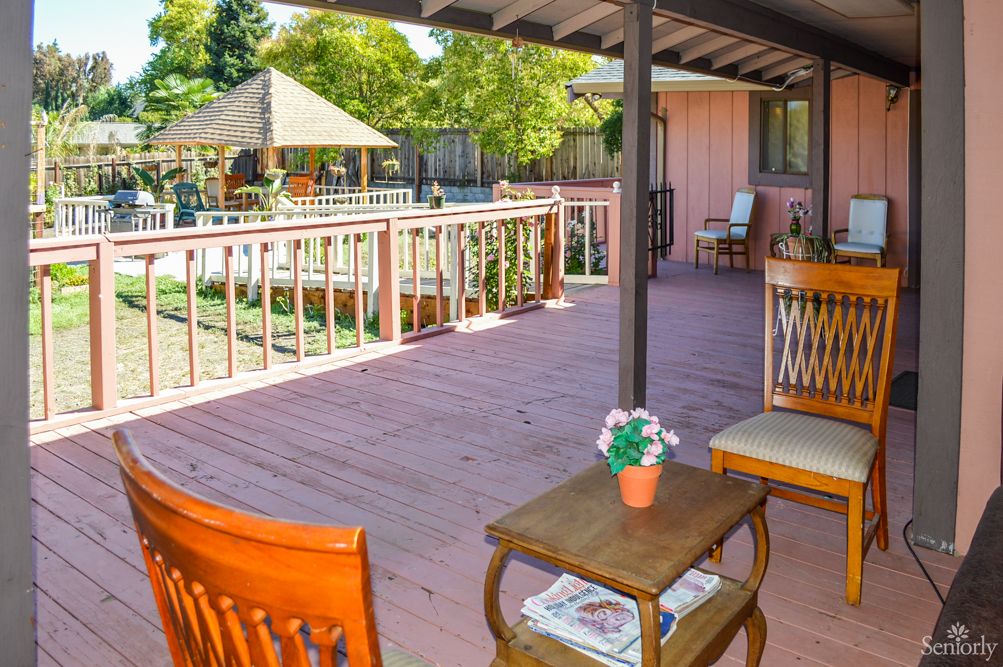 A spacious outdoor patio with wooden furniture overlooking a garden area.