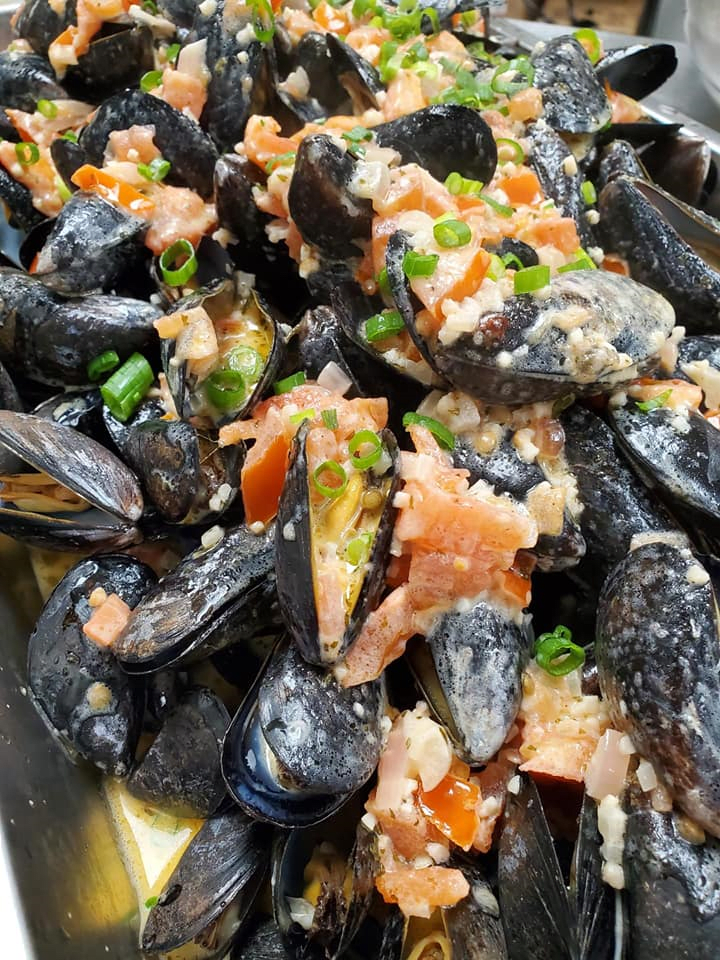 A dish of cooked mussels garnished with tomatoes and green onions.