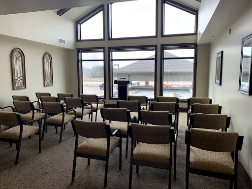A vacant meeting room featuring rows of chairs and a podium, illuminated by natural light from large windows.