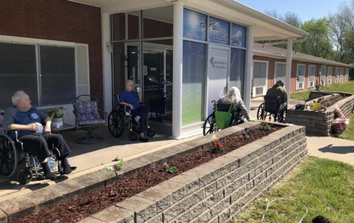 Elderly individuals sitting in wheelchairs outside a nursing home during the daytime.