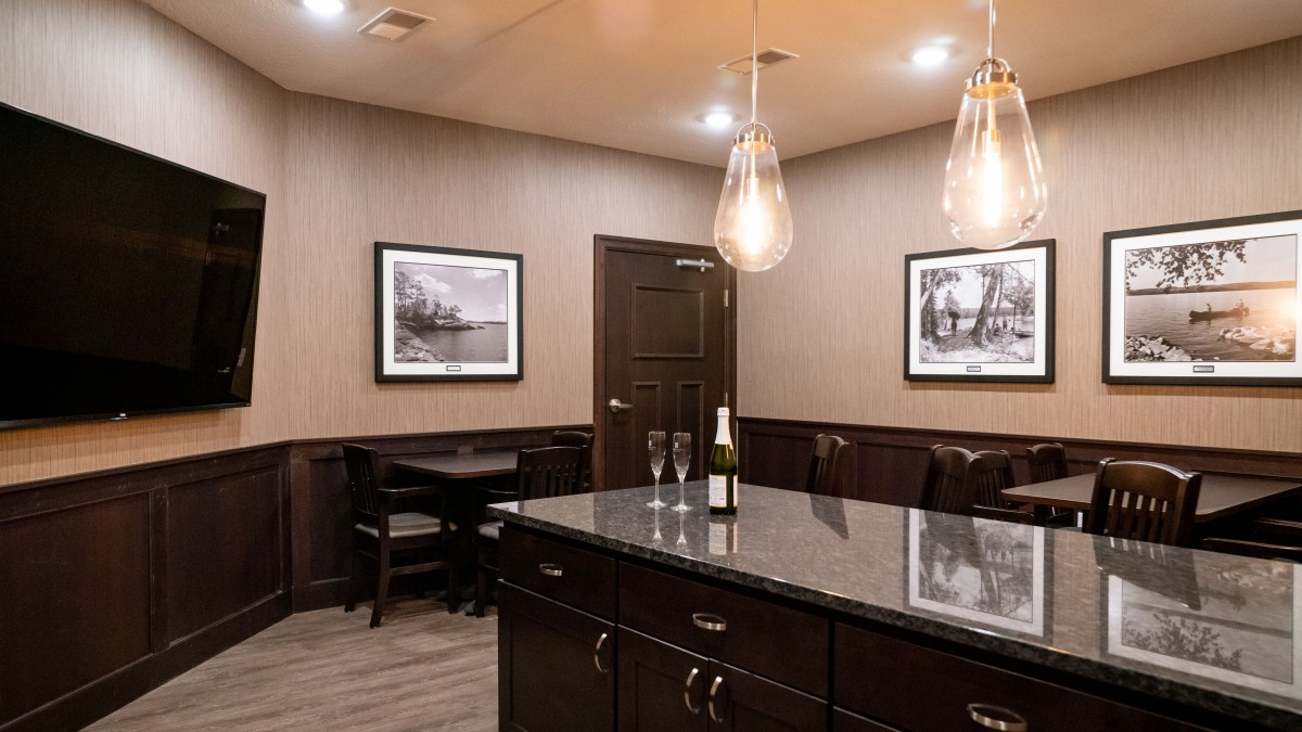A modern kitchen interior featuring a large island with a wine bottle and glasses, illuminated by pendant lights and decorated with framed artwork.
