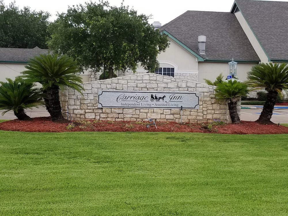 Entrance sign of a gated community with surrounding greenery and a building in the background.