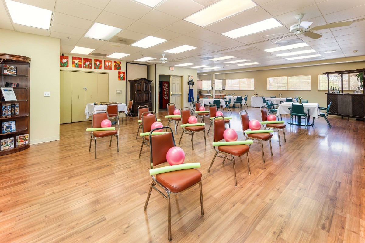 A brightly lit exercise room with chairs arranged in rows, each topped with a balloon and pool noodle.