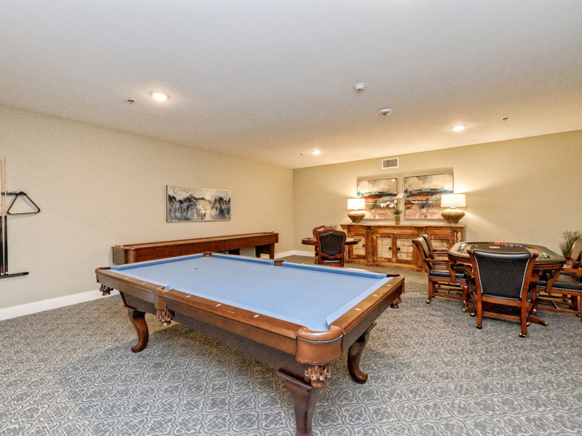 A well-lit game room featuring a blue felt pool table and stylish furniture.
