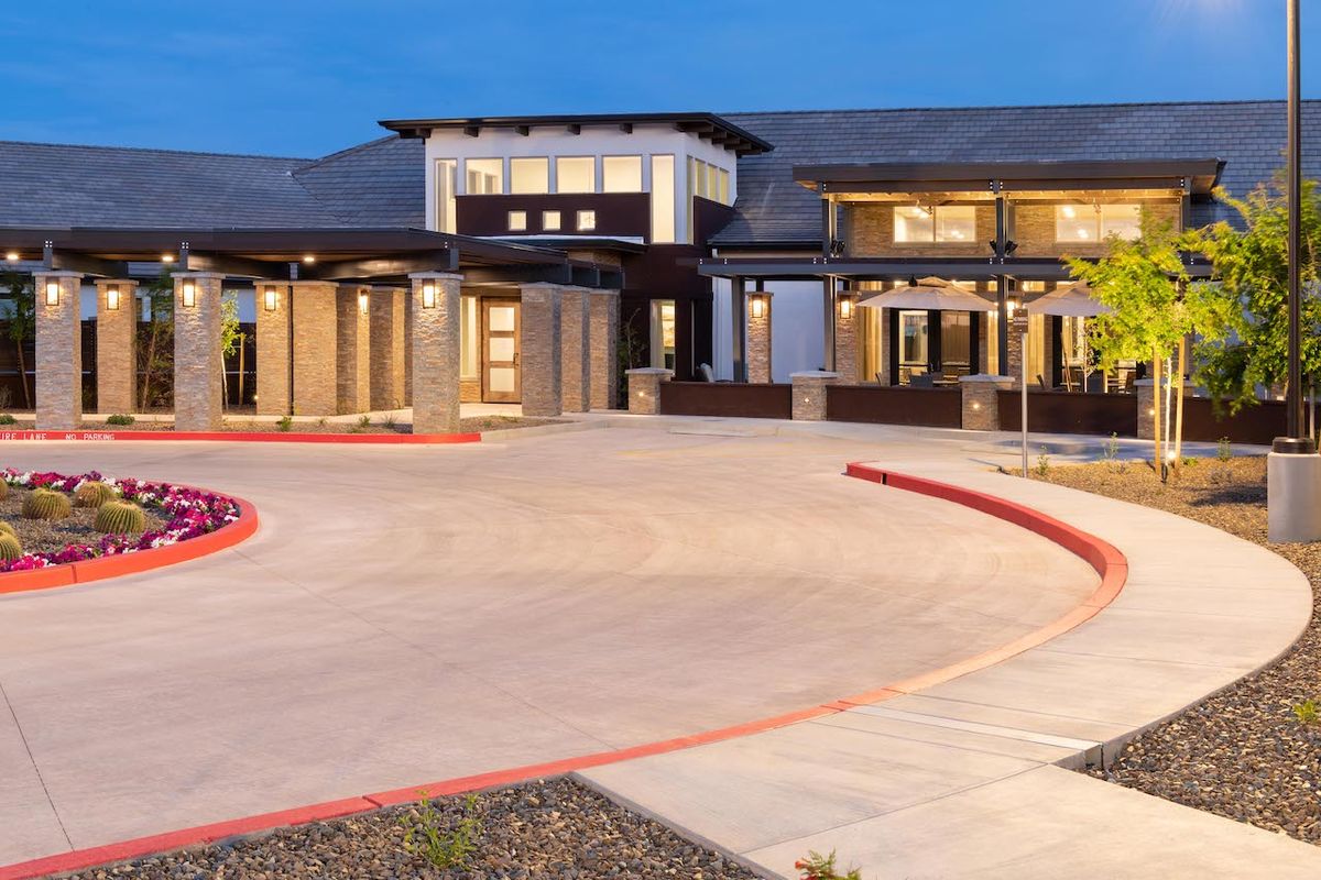 A modern building with a well-lit driveway in the evening.