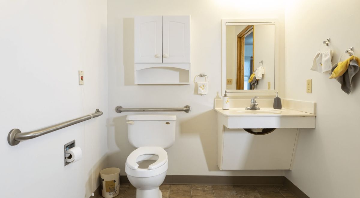 An accessible bathroom featuring a toilet, sink, mirror, and grab bars for safety.