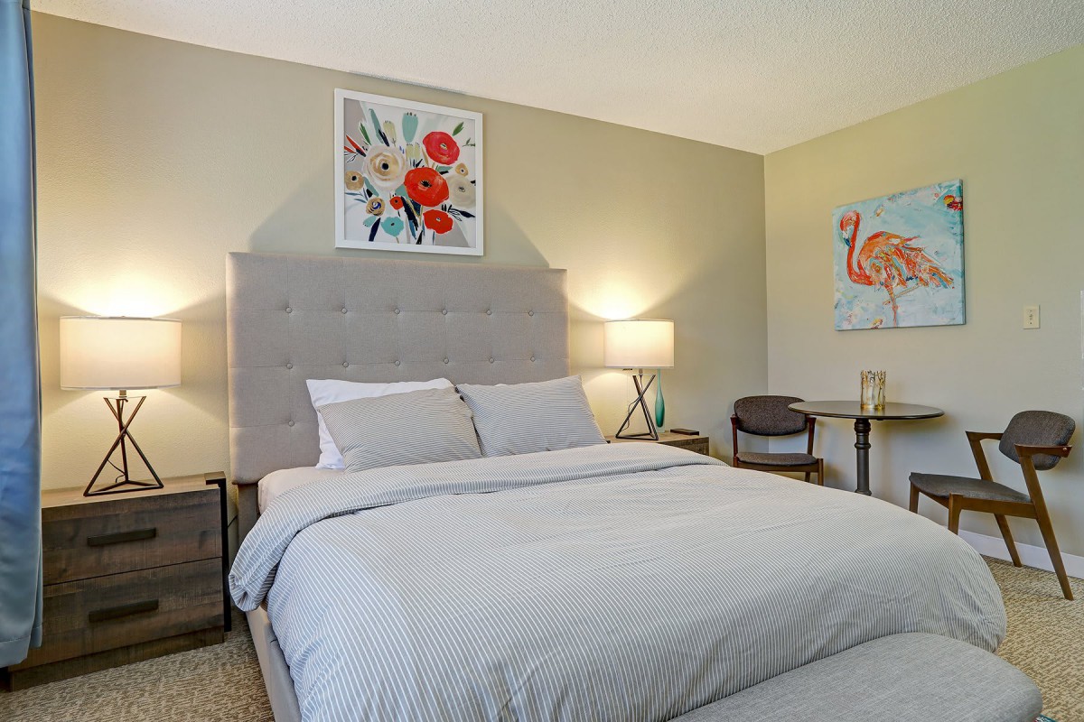 A cozy bedroom with a neatly made bed, two bedside lamps, and artwork on the walls.