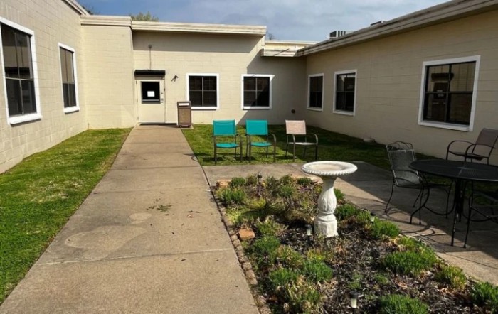 A view of an outdoor area featuring a pathway, garden, and chairs in front of a building.