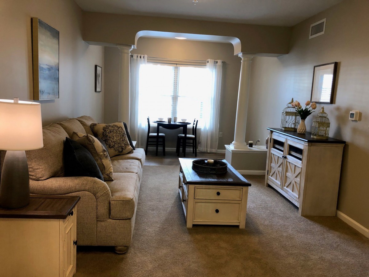 A cozy living room with a sofa, coffee table, and adjacent dining area, featuring warm lighting and elegant decor.