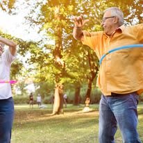 Two seniors having fun with hula hoops in a sunny park.