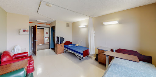 A simple and clean patient room in a hospital, equipped with a bed, desk, and television.