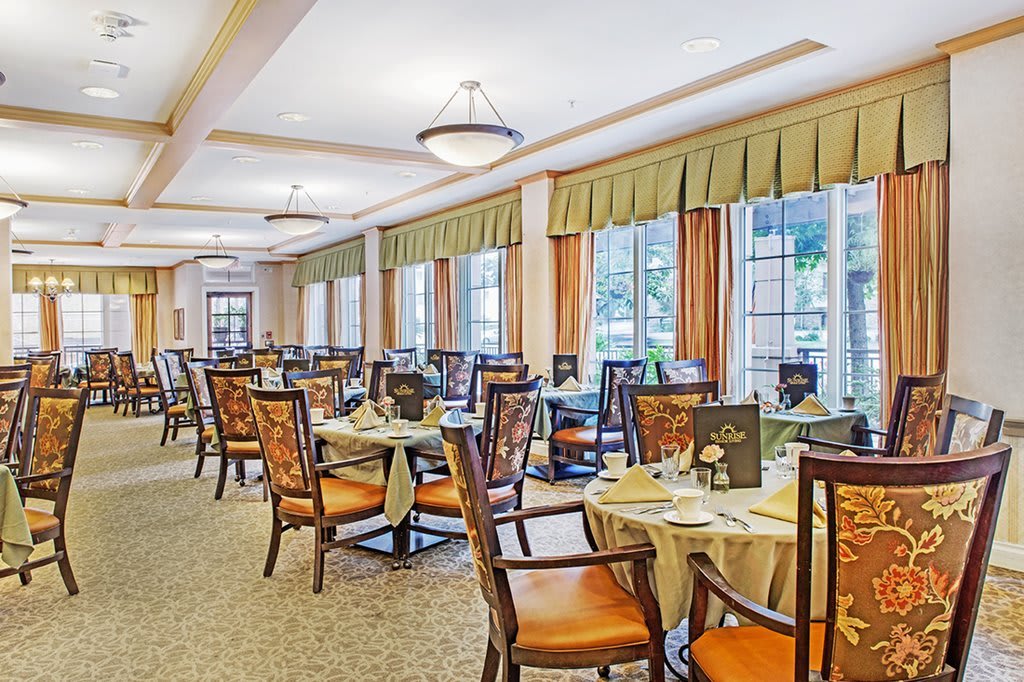 An elegant dining room with neatly arranged tables and chairs, featuring large windows allowing natural light.
