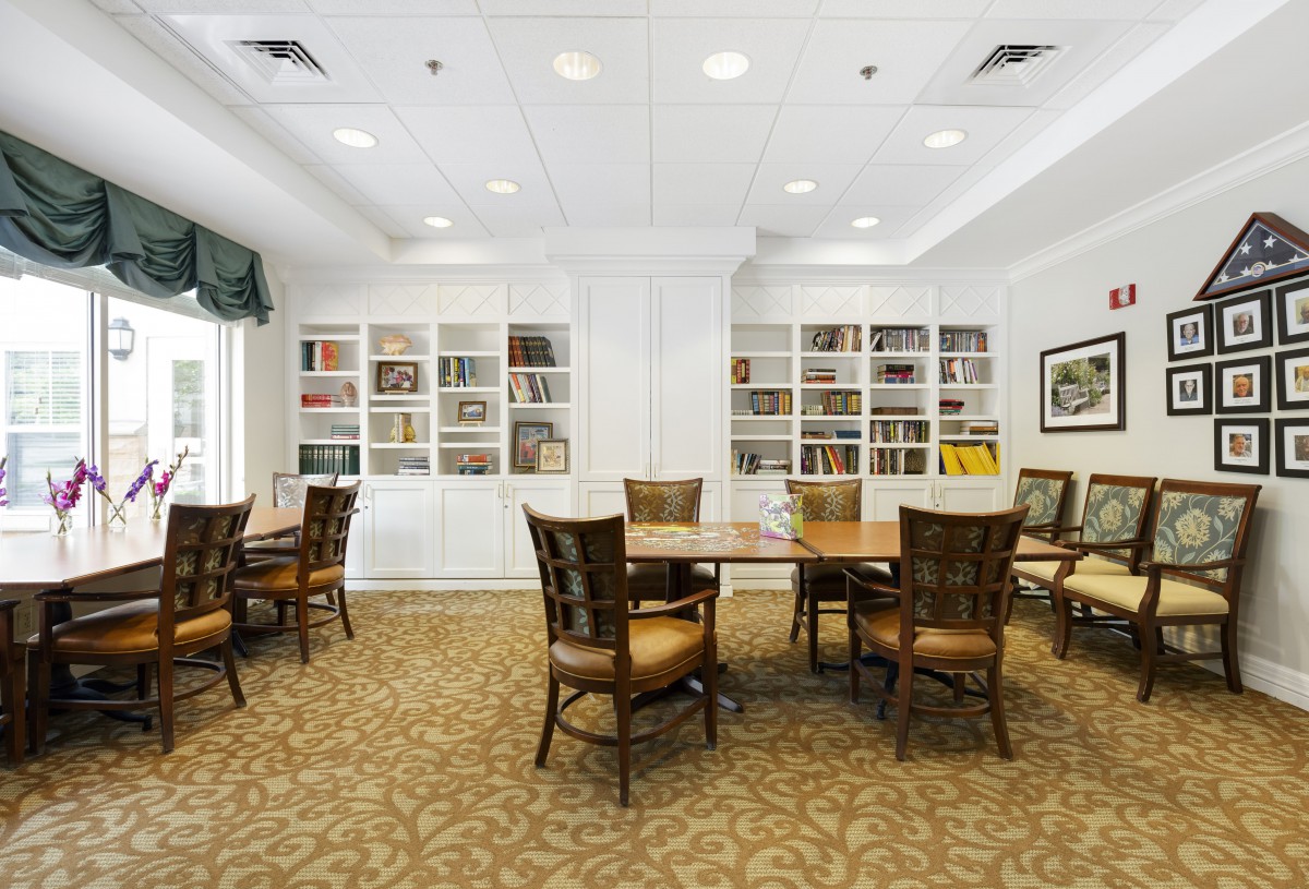 A cozy library interior with tables and chairs for reading or meetings, surrounded by bookshelves.