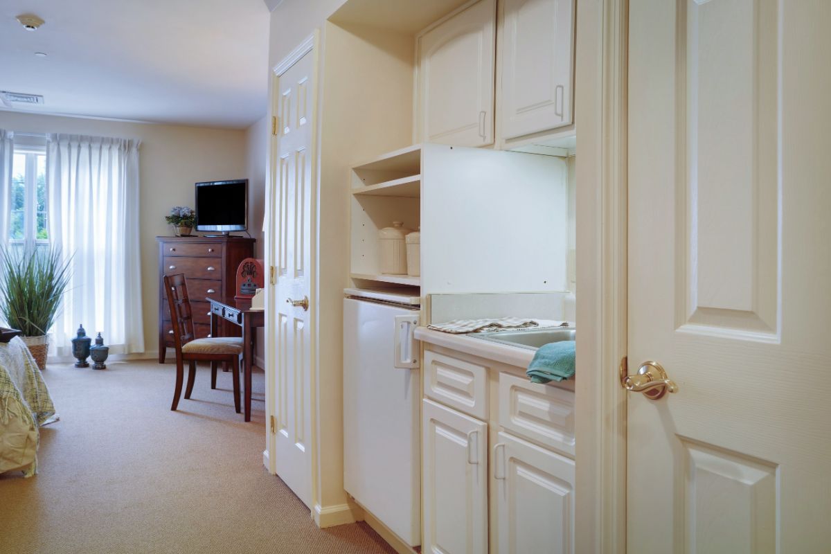 A compact kitchen area opens up to a hallway leading to a living space with a dining table and television.
