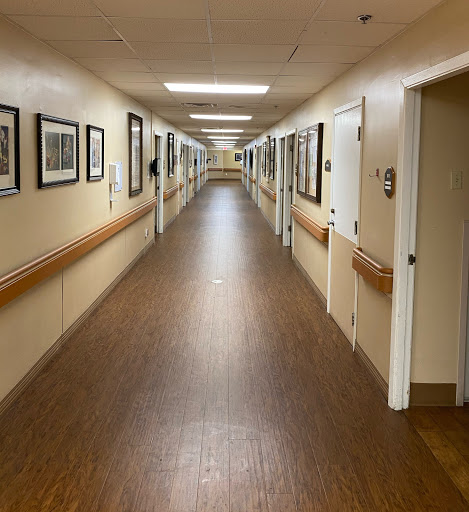 A well-lit corridor lined with photographs, featuring a wooden floor and multiple doors on either side.